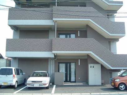 3階建ての介護施設の建物外観。駐車場に複数台の車が停まっている。