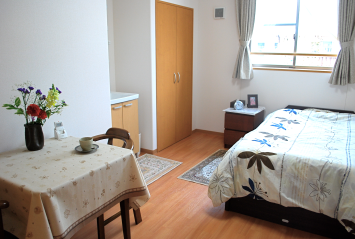 居室内の生活空間。テーブル、ベッド、収納が配置された個室